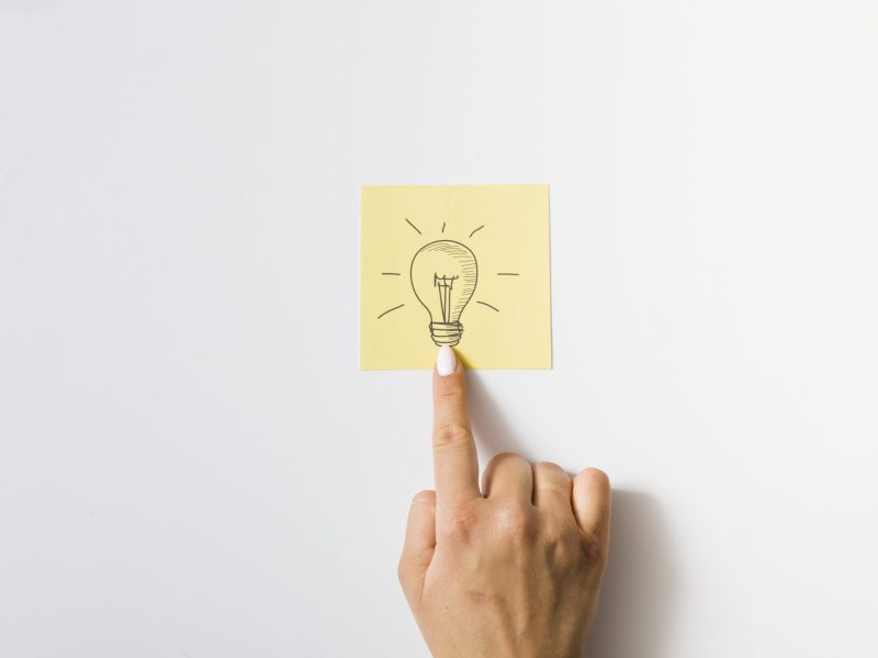 close-up-person-touching-finger-drawn-light-bulb-sticky-note